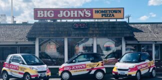 The outside of Big John's Pizza in Pendleton, Oregon. In the photo there are several little white delivery cars for Big John's parked out front.