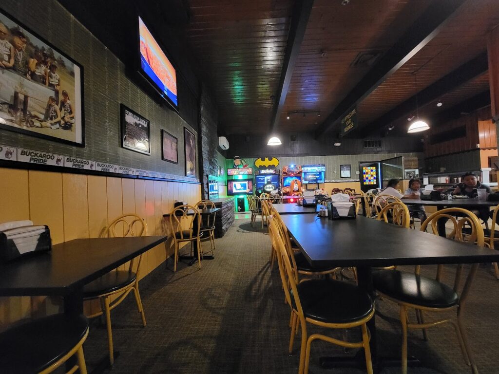The inside of Big John's Pizza in Pendleton, Oregon. There's a dark wood ceiling, black tables and wooden chairs. There are a few arcade games against one wall.