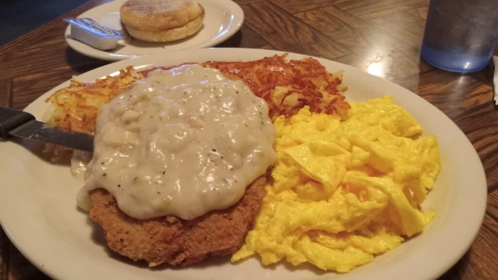 Chicken fried steak with country gravy, hash browns and scrambled eggs on a plate.