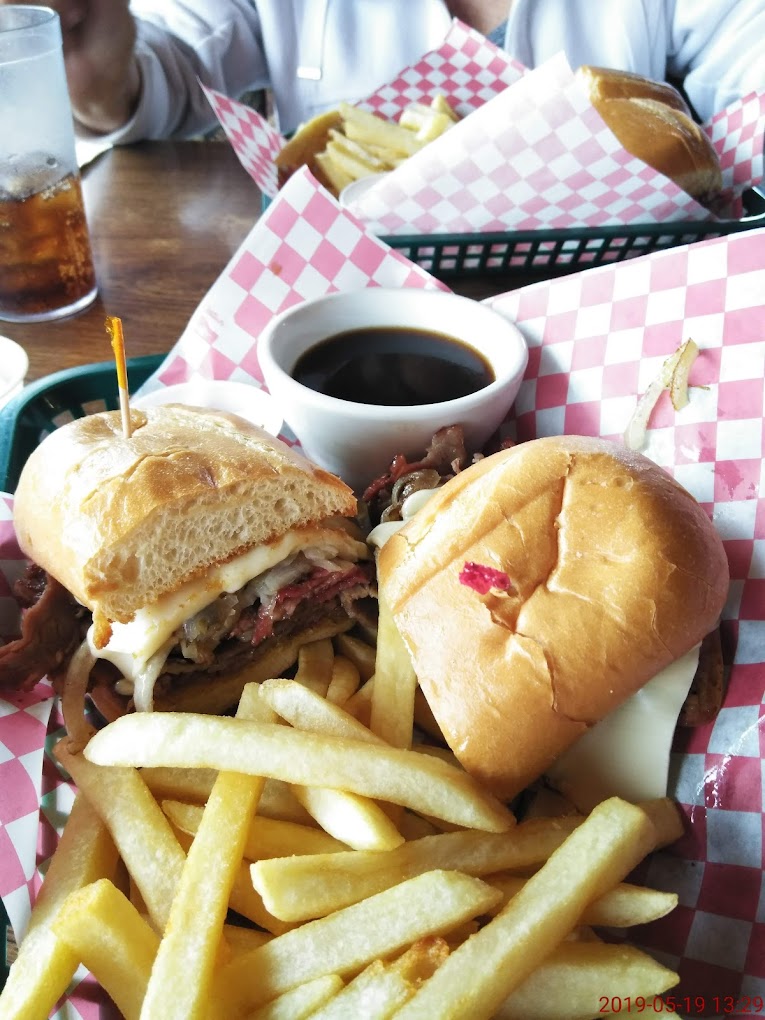 A super delicious looking sandwich with steak and cheese and what looks to be au jus dip. There are fries with it on a red and  white checkered paper wrapper.