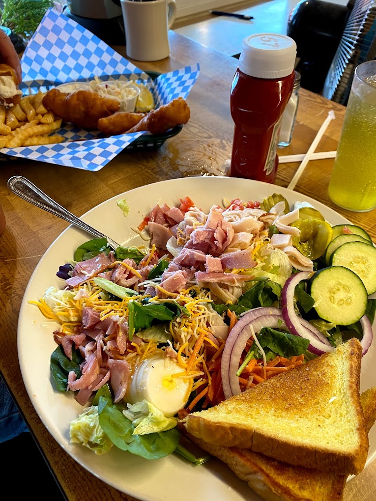 A large salad with all kinds of good stuff and a piece of toast. The salad looks to have ham, egg, cucumber, red onion, and a variety of other things! It looks tasty!