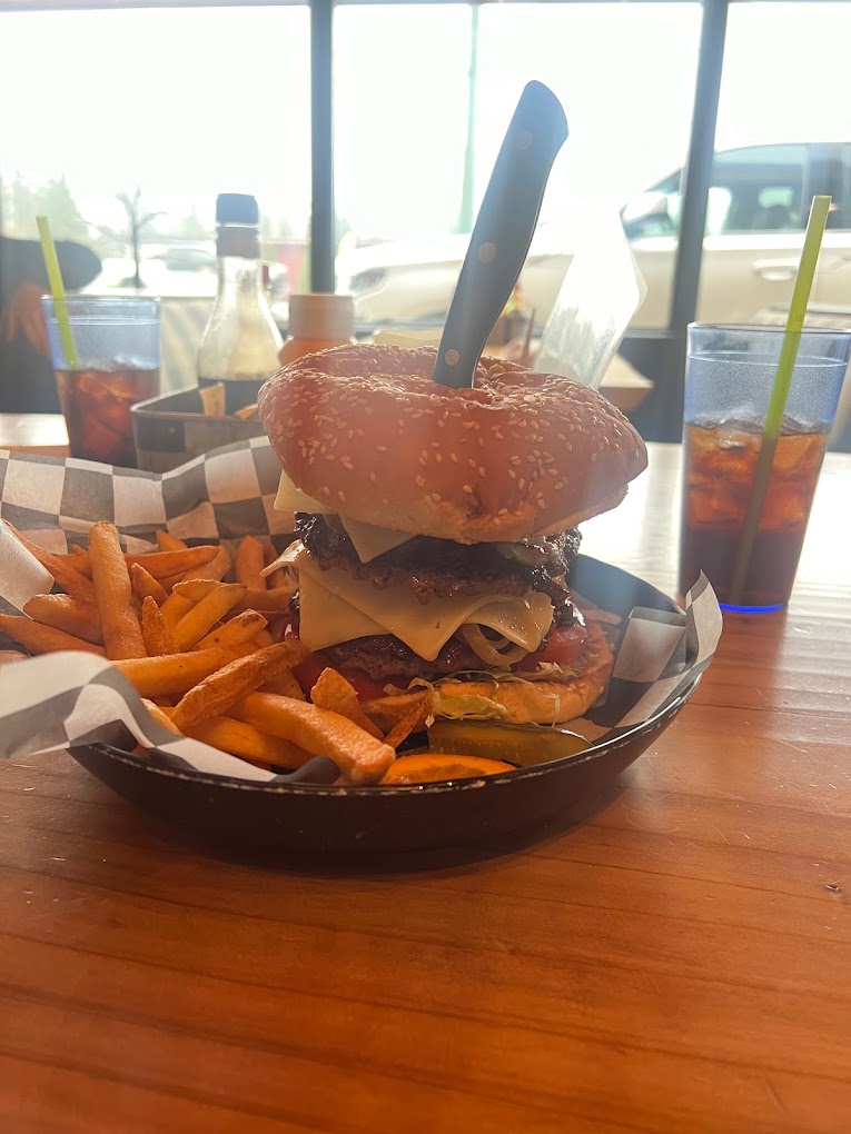 A really big burger with a knife sticking out of the top of it to hold it together. There are sweet potato fries on the side.