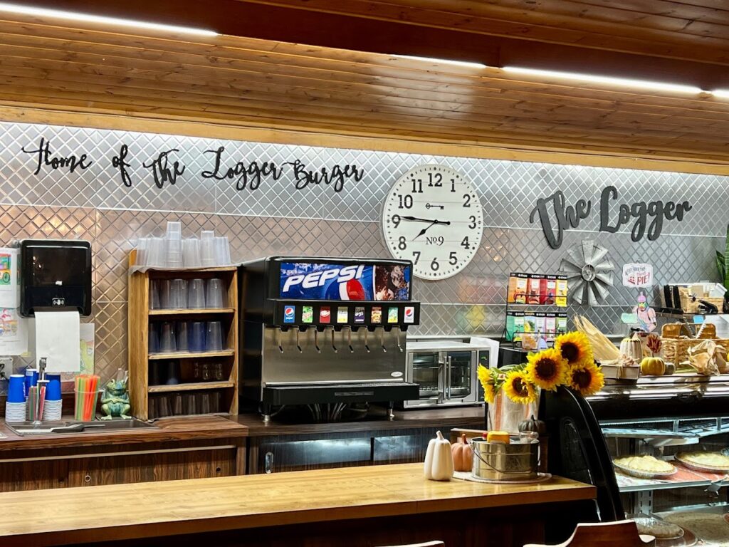 The cute interior of The Logger Restaurant. Part of it has a metal wall with cute cursive letters in black metal, and a large round white clock. There are sunflowers on display on the counter.