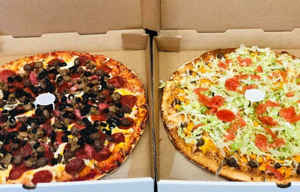Two pizza's sitting side by side, each in their own pizza box with the lid open.