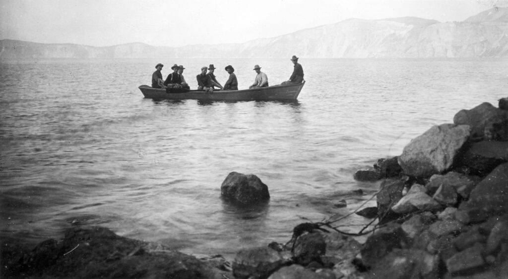 An old black and white photo of 8 men on a boat on the waters of Crater Lake, Oregon.
