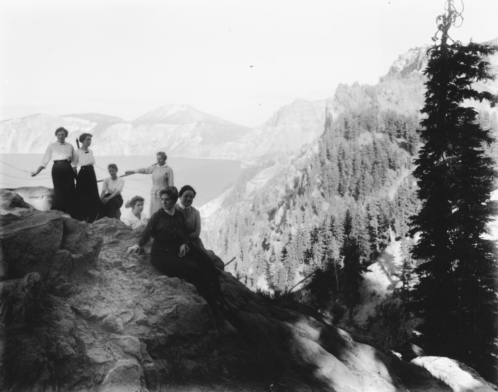 An old historic black and white photo of seven women on the rim at Crater Lake.