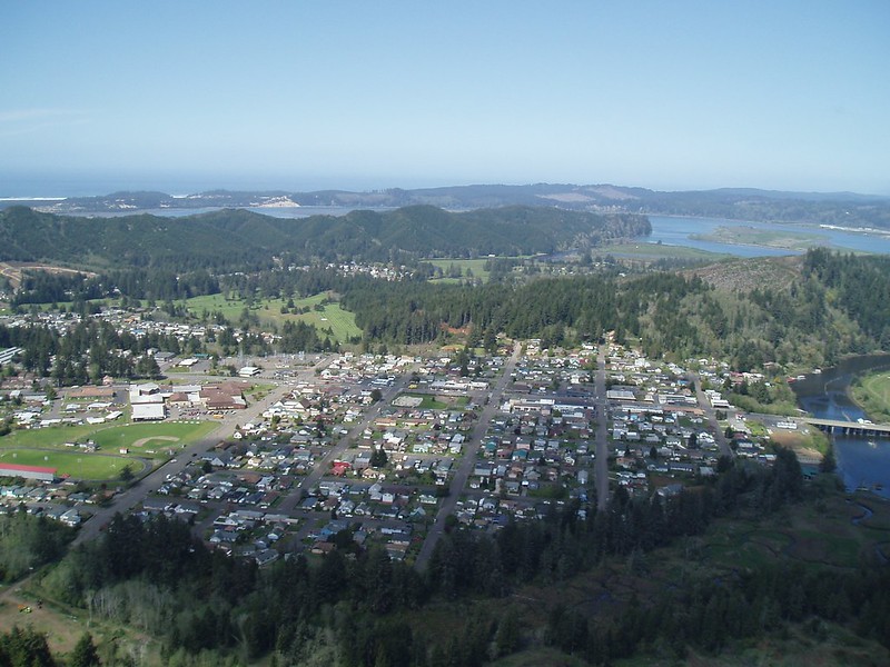 An aerial view of Reedsport and the Umpqua River. The city is surrounded by forest.