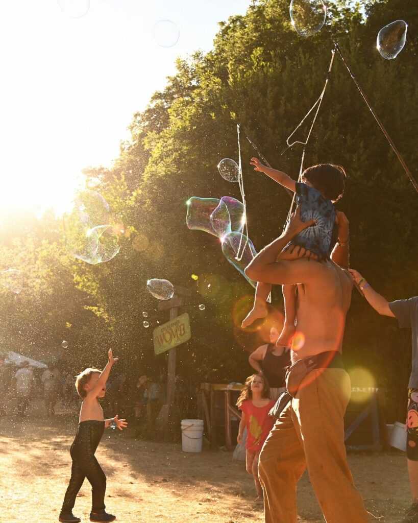 Children and an adult playing with bubbles in the warm evening light.