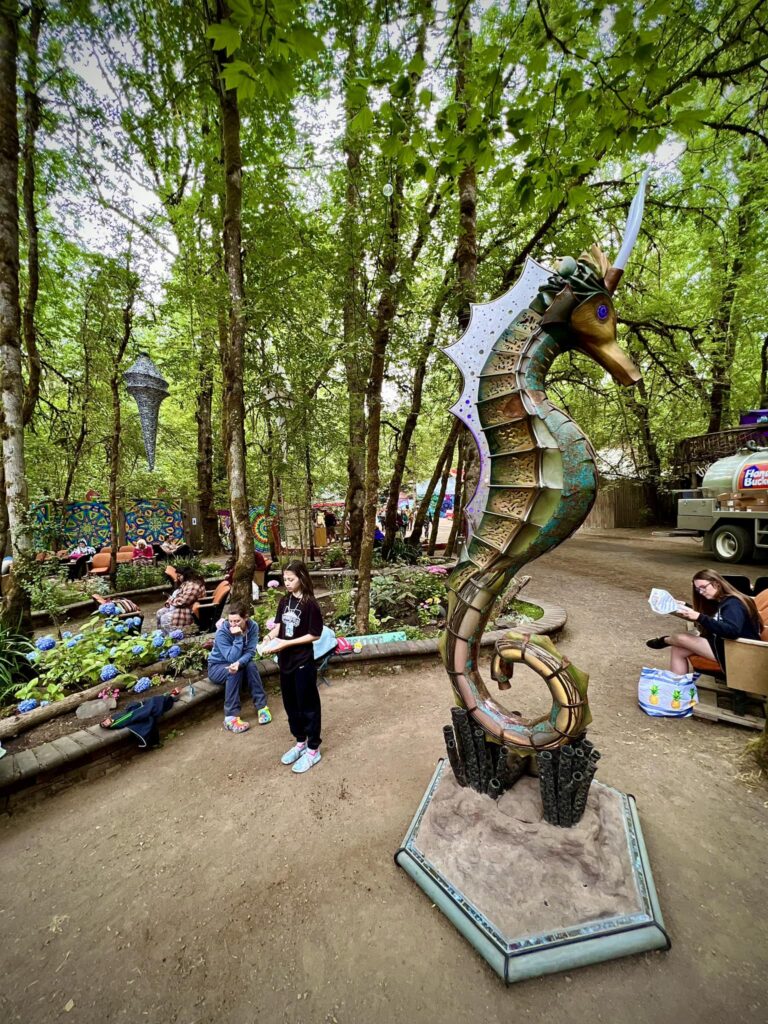 People in a shaded forest area enjoying a large seahorse statue.