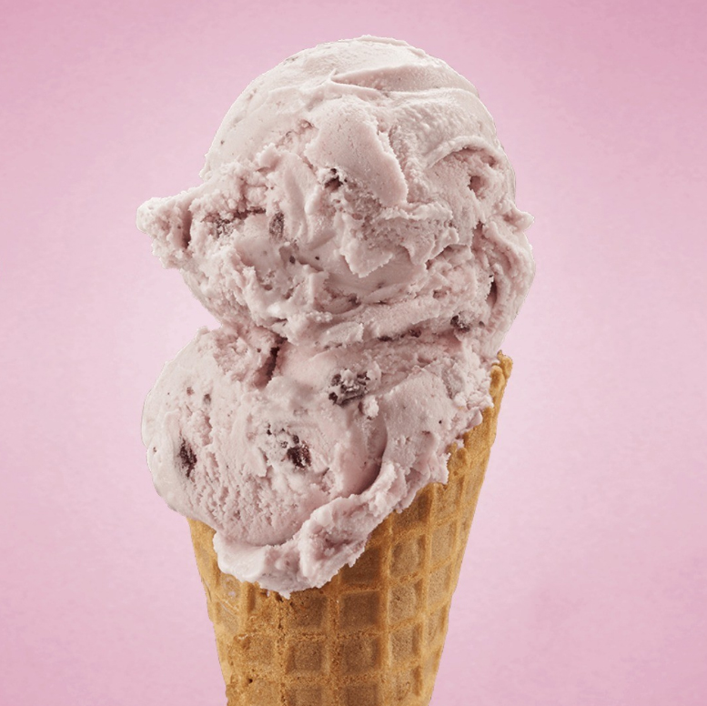 Light pink ice cream in a small waffle cone. The photo has a light pink background.