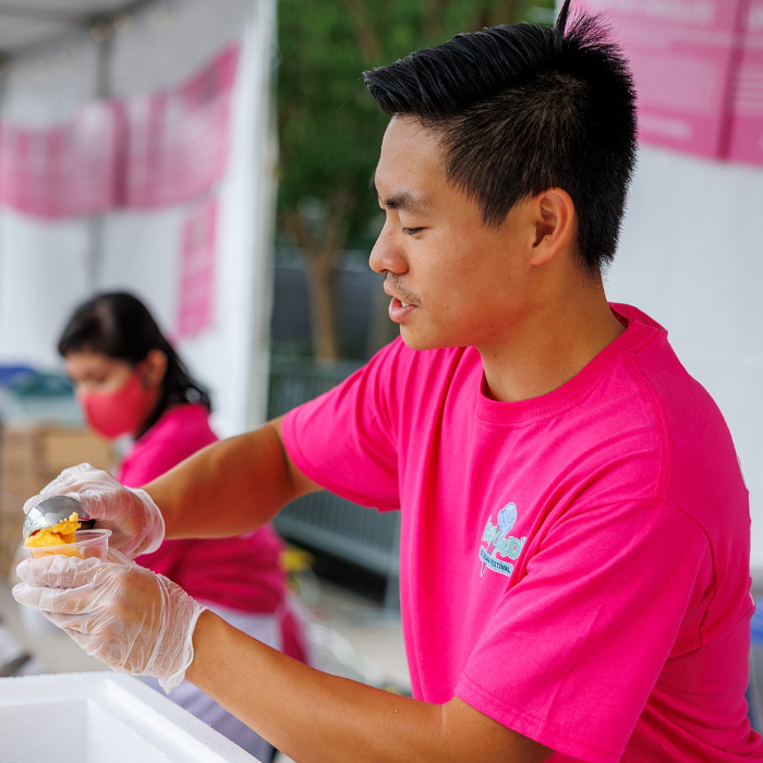 A man in a hot pink shirt scoops ice cream into a small plastic cup.