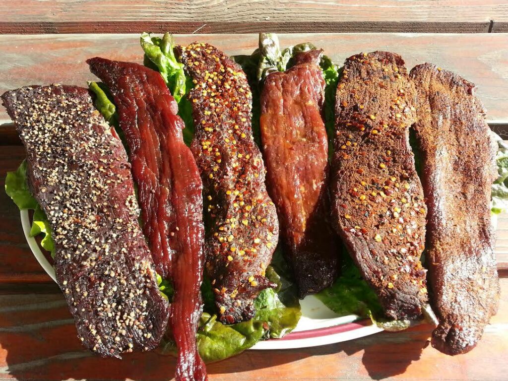 A variety of fresh smoked jerky lined up next to each other.