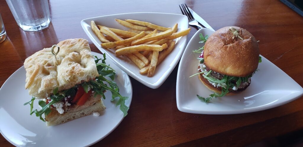 A tasty looking burger, a good looking sandwich, and fries. The fries are on an interestingly shaped white triangle plate.