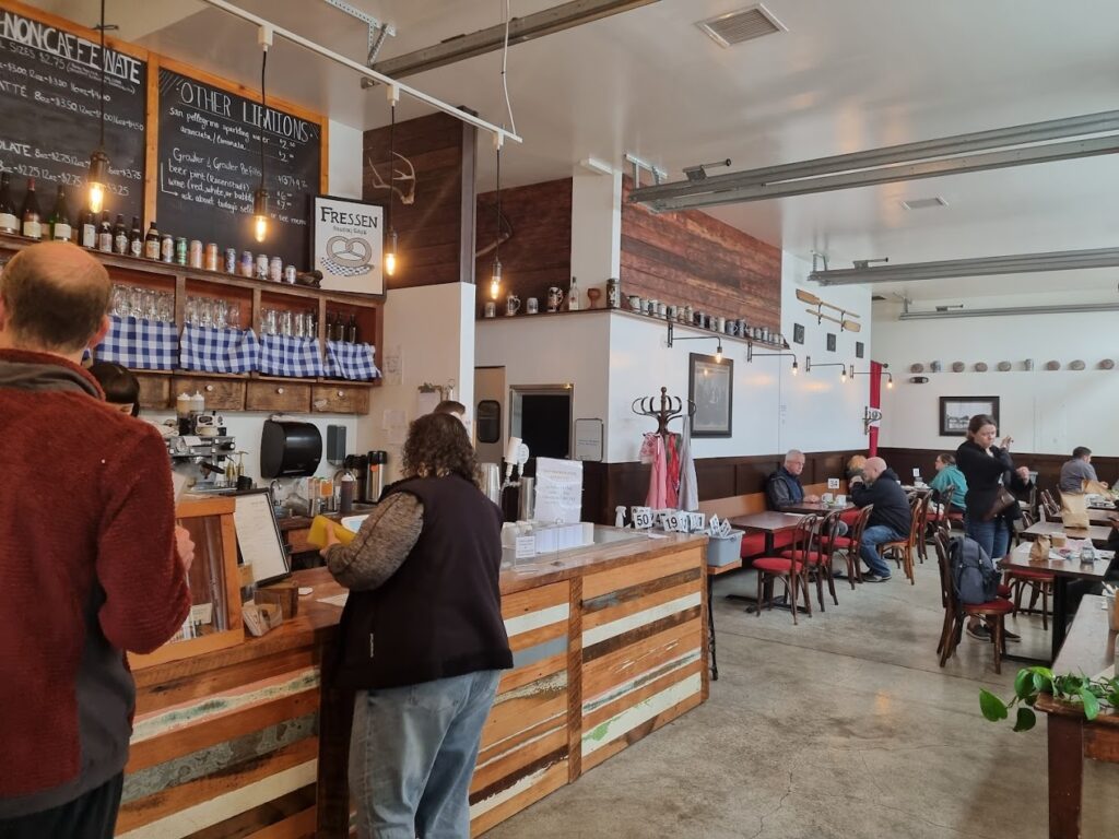 The interior of Fressen Artisan Bakery in Portland, Oregon. It has a very cozy feel inside. People order at the counter, or sit and enjoy their food at tables. There are high ceilings and wooden accents around the bakery.