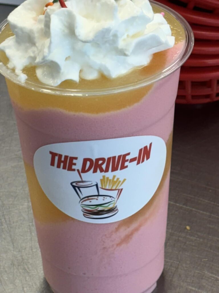 A cold, sweet drink topped with whip cream in a clear cup. The drink is yellow and pink.