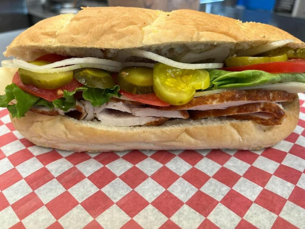 A tasty looking sandwich with pickles, onions, meat, lettuce, and other toppings.