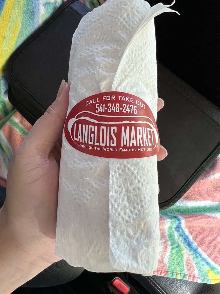 A famous Langlois Market hot dog, wrapped up in a paper food wrapper and a paper towel with a red Langlois Market sticker.