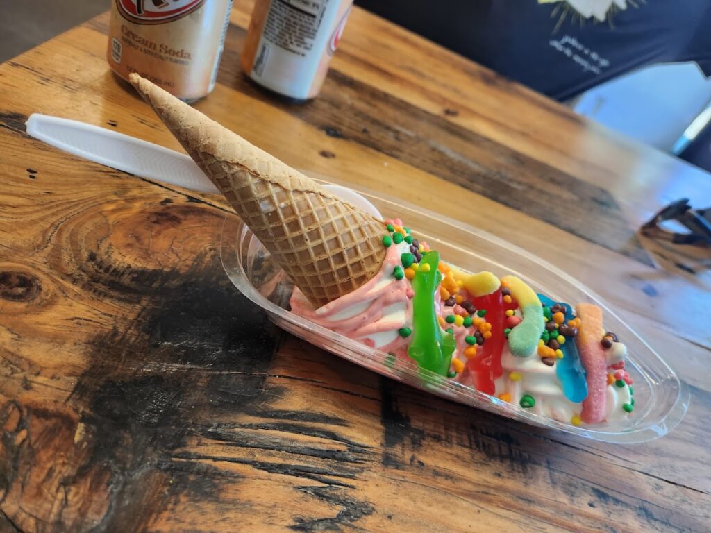 A crazy looking ice cream treat spread out in a dish, covered in toppings, with an upside down waffle cone on top. Looks good!