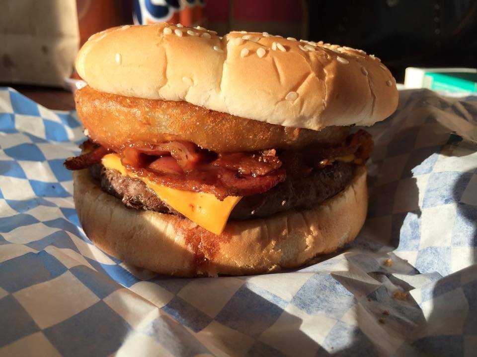 A burger with cheese and an onion ring on blue and white checkered paper.