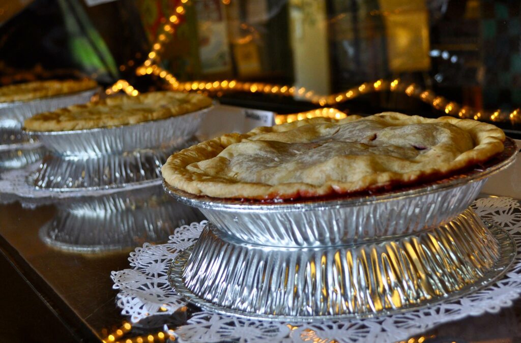 Several pies in metal pie tins. Orange string lights light up the display case that the pies sit inside of.