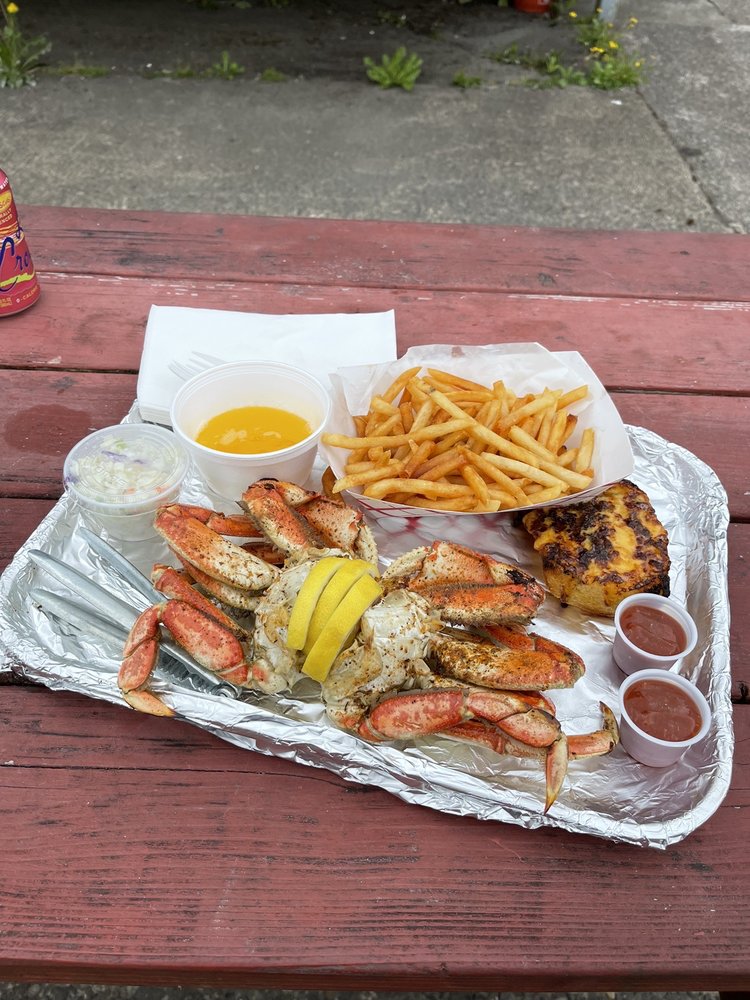 A tray full of crab, fries, and sauces to dip the crab in on a red picnic table.