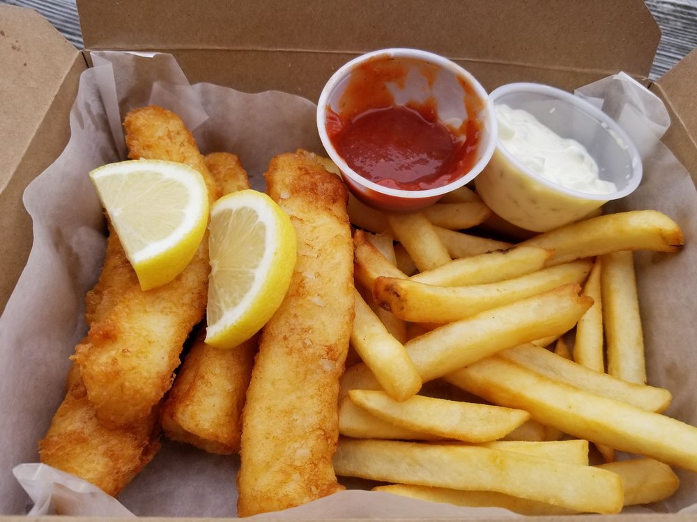 Halibut fish and chips with dipping sauce, two slices of lemon, and French fries.