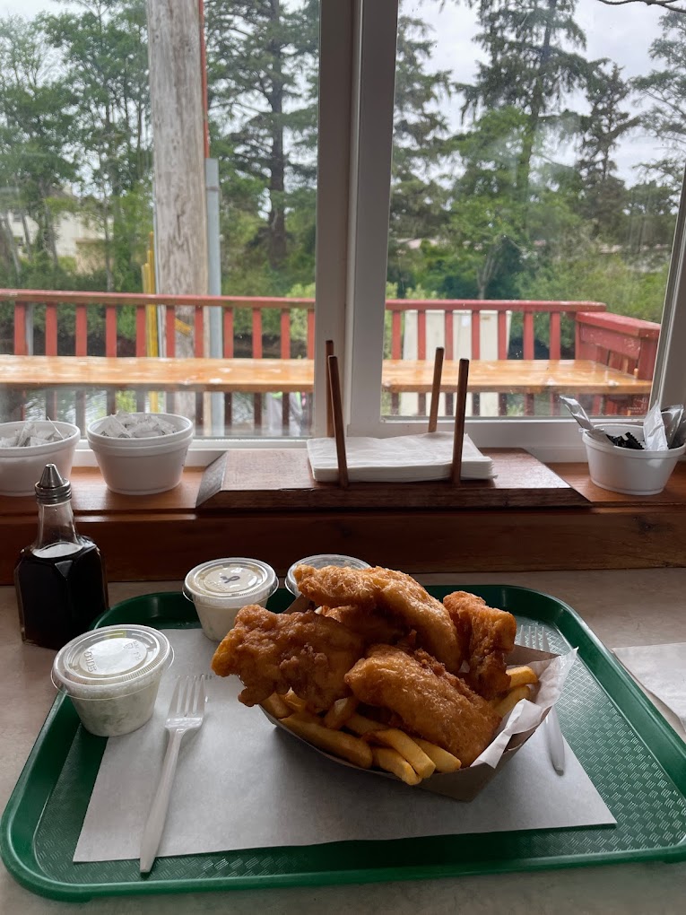 Fried seafood on top of fries in a basket on a green tray. The food is in front of a window looking out onto the back deck and river.