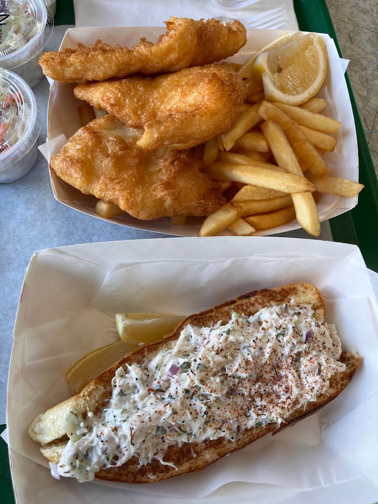 A seafood sandwich and a basket of fried seafood and fries with a small container of coleslaw.