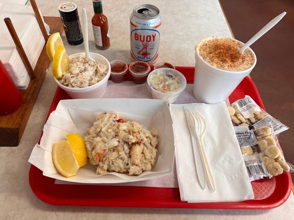 A red tray full of all kinds of seafood and a tall white container of chowder.