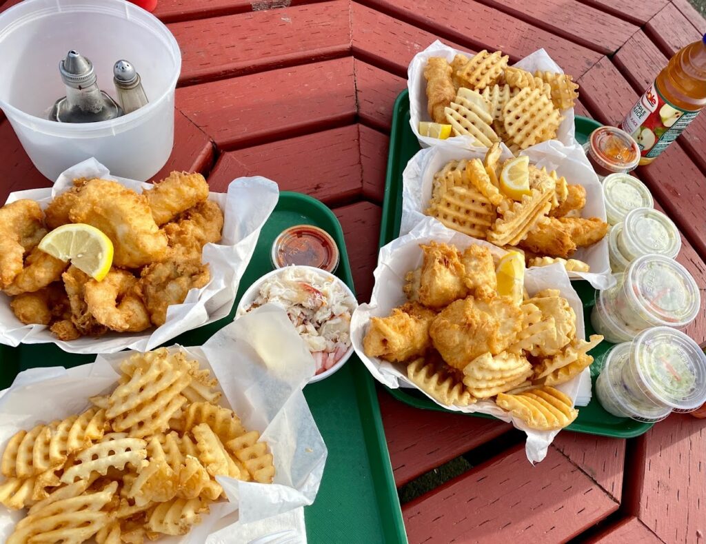 Two green trays full of seafood and waffle fries on a red picnic table.