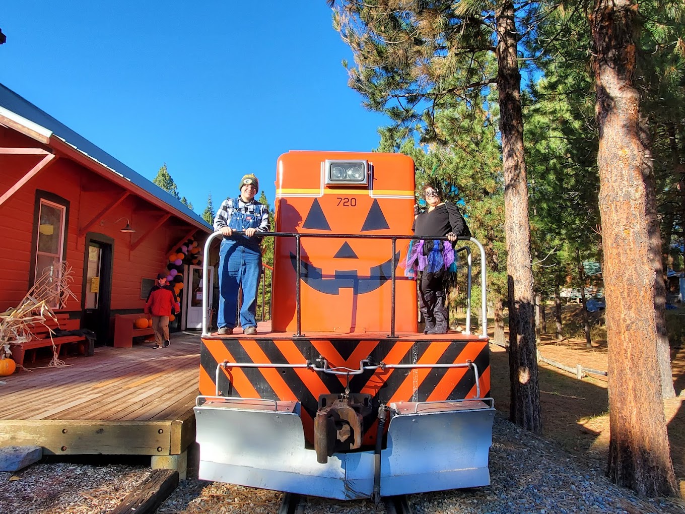 Two people stand on an orange train painted to look like a jack-o-lantern