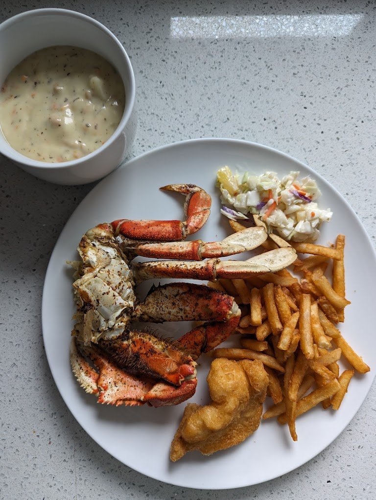 A white plate with crab, fries, and coleslaw. There's a white bowl of chowder next to it.