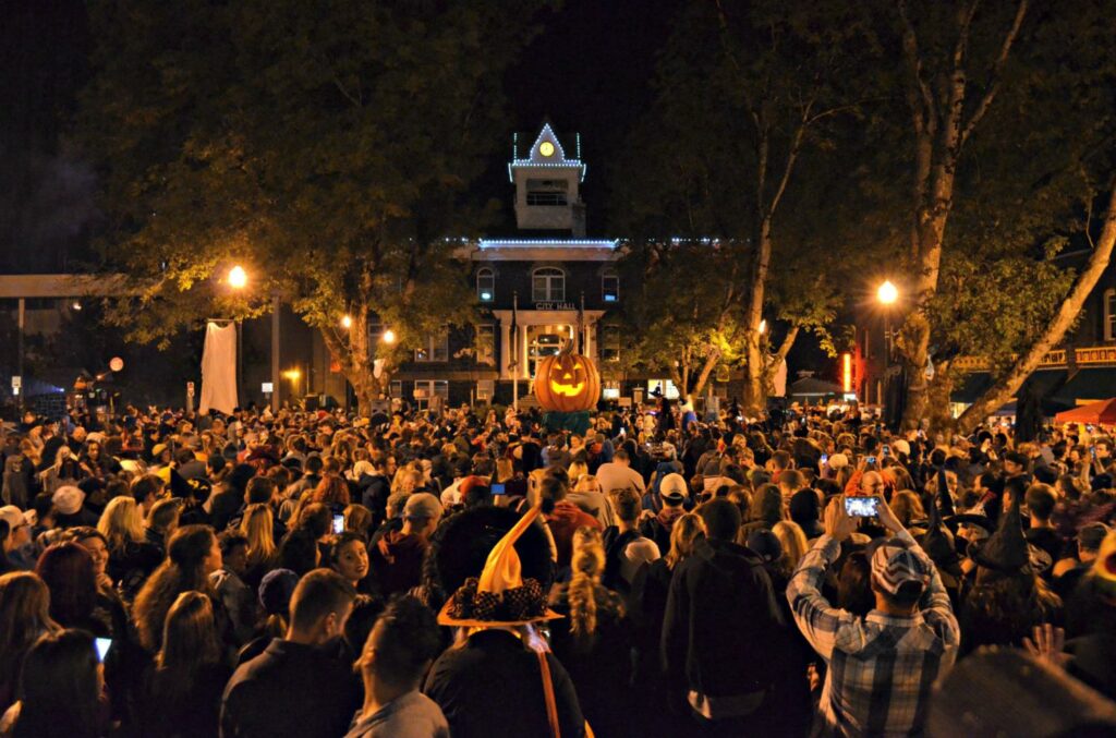 A crowd gathers in front of a massive pumpkin at night.