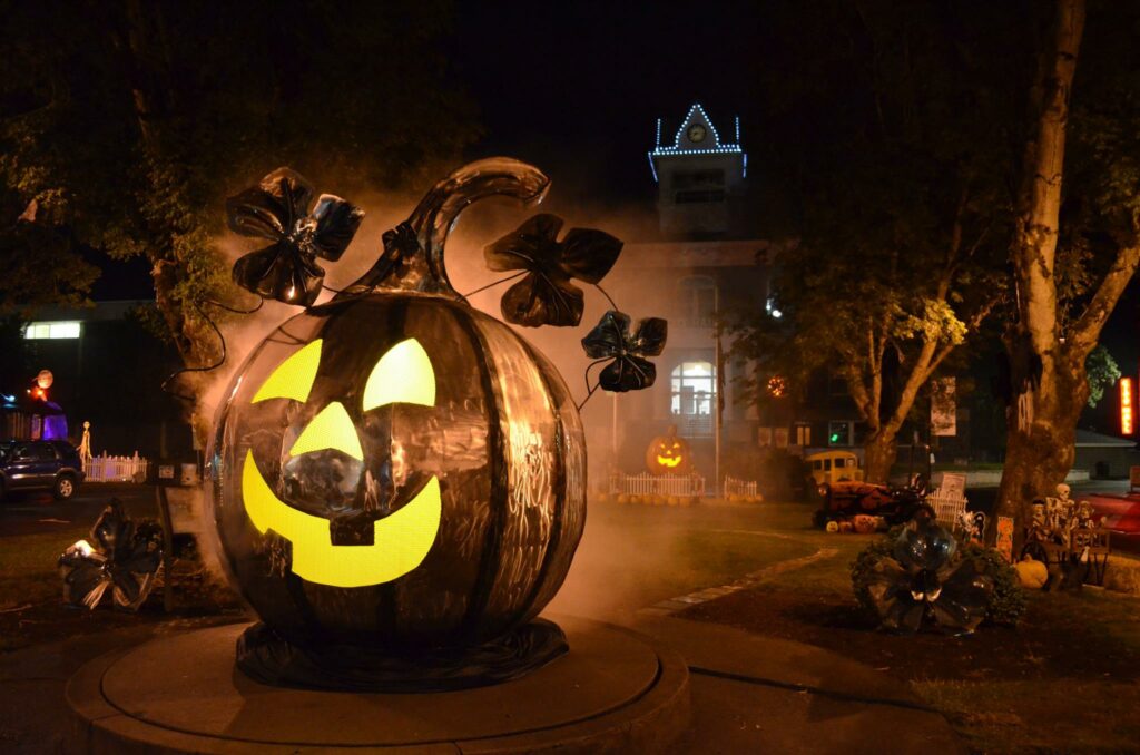 A large metal pumpkin lit up at night.