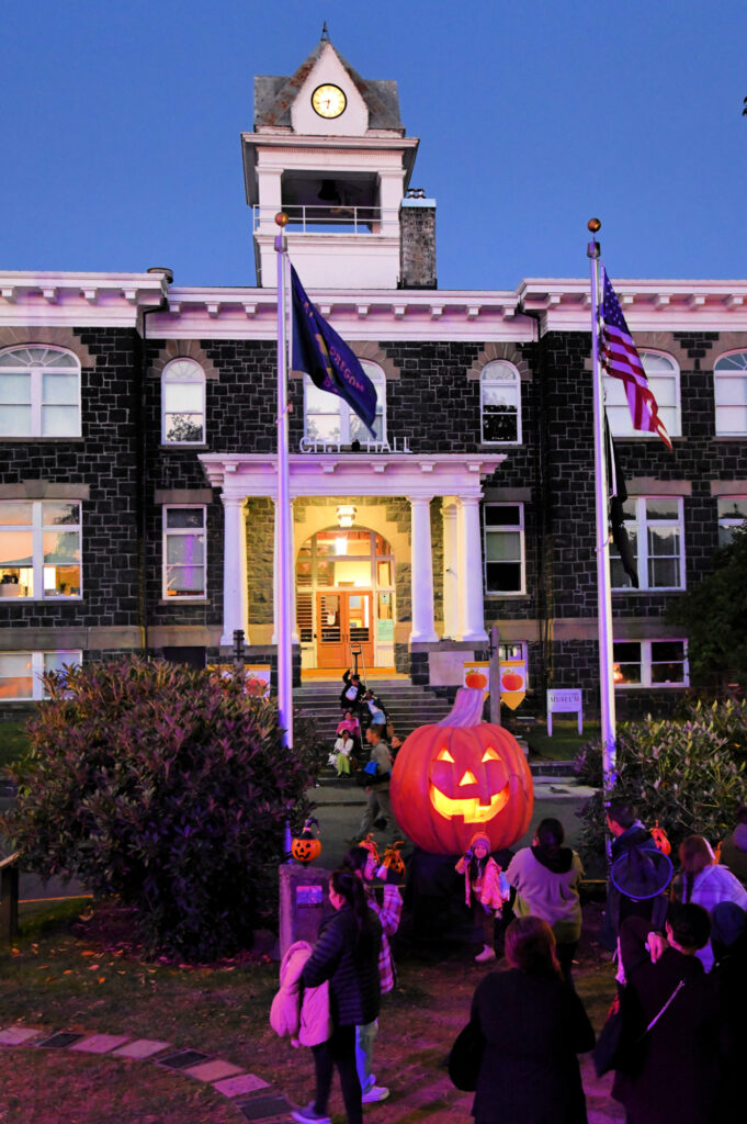 A crowd gathers in front of a massive pumpkin at night.