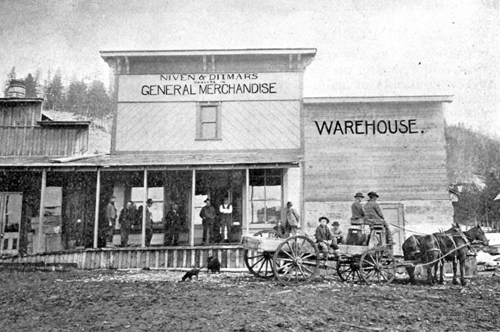 A black and white photo of many people sitting in front of a general merchandise store and warehouse in what is now the ghost town of Granite, Oregon.