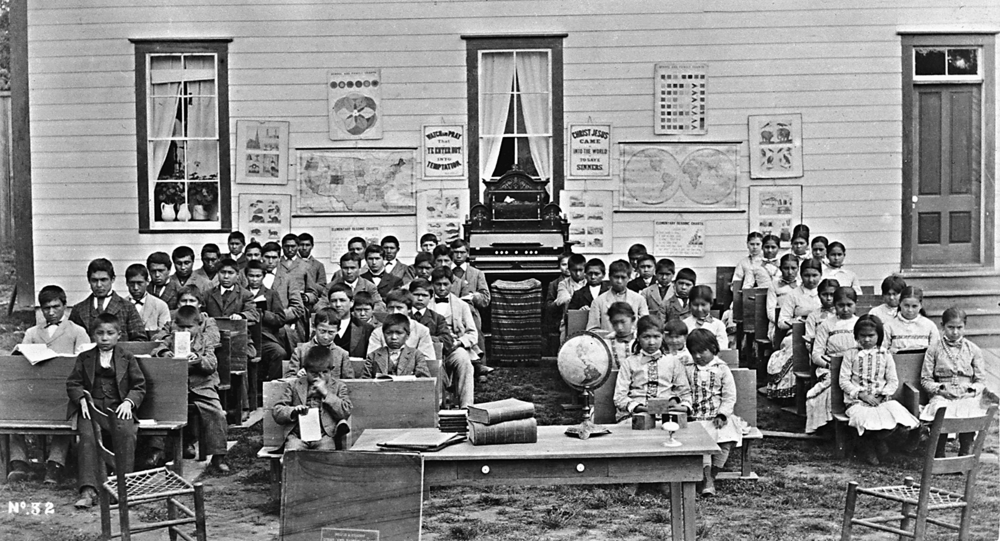 Students stand for a photo in front of the school in Indian Training School in Forest Grove. Many of them are young and look unhappy.