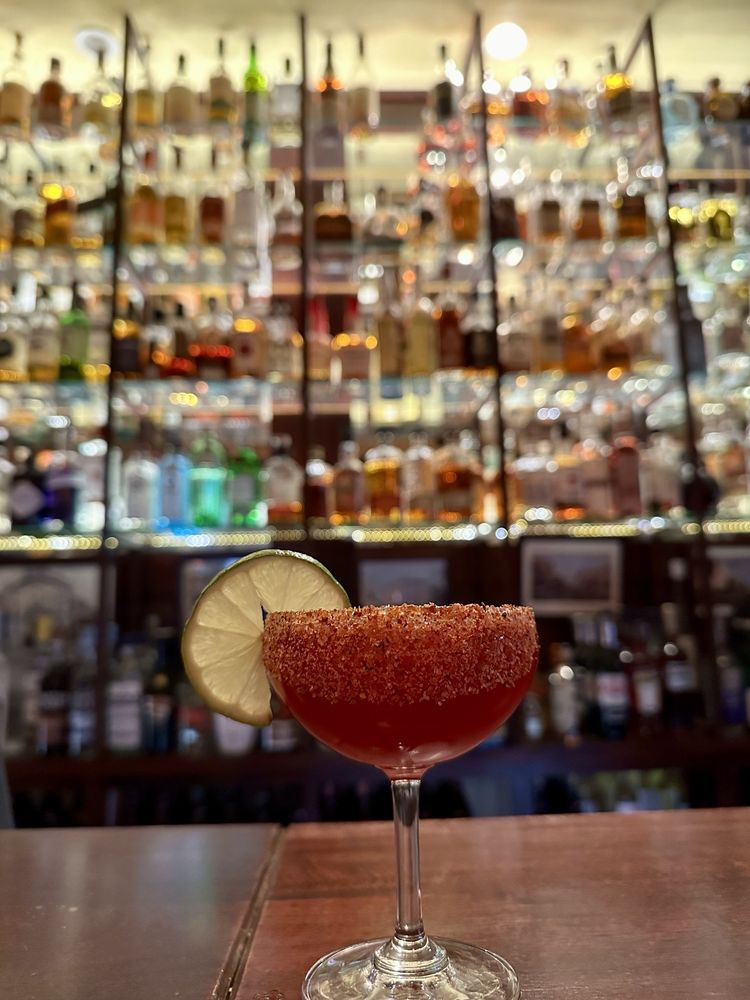 A colorful drink at La Rambla in front of a wall of glass bottles of alcohol.