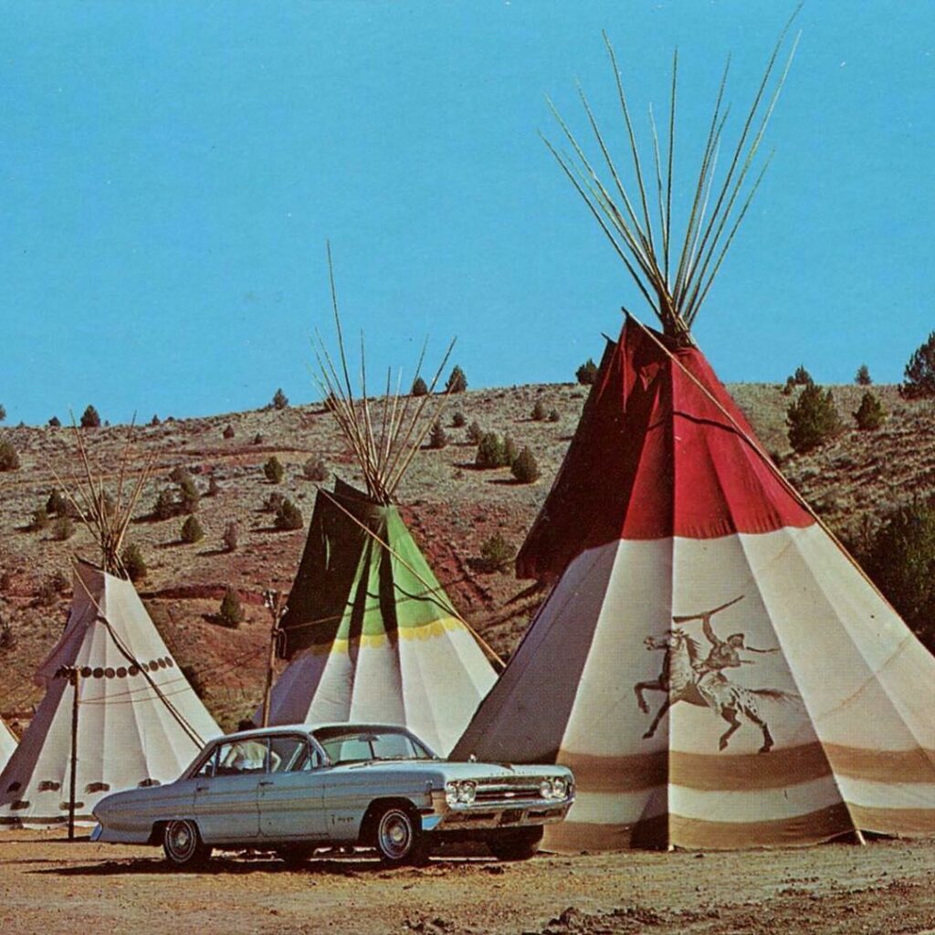 An old photo oft he old teepees at Kah-Nee-Ta. A classic car sits out in front of three teepees.