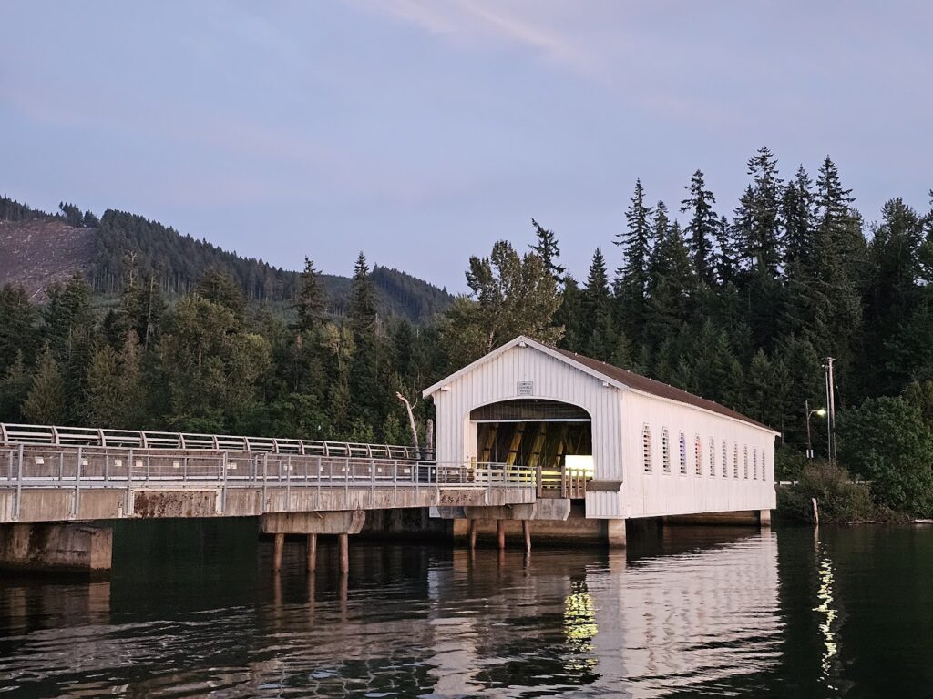 The Lowell Covered Bridge in the evening. Calm waters flow beneath the white wooden bridge.