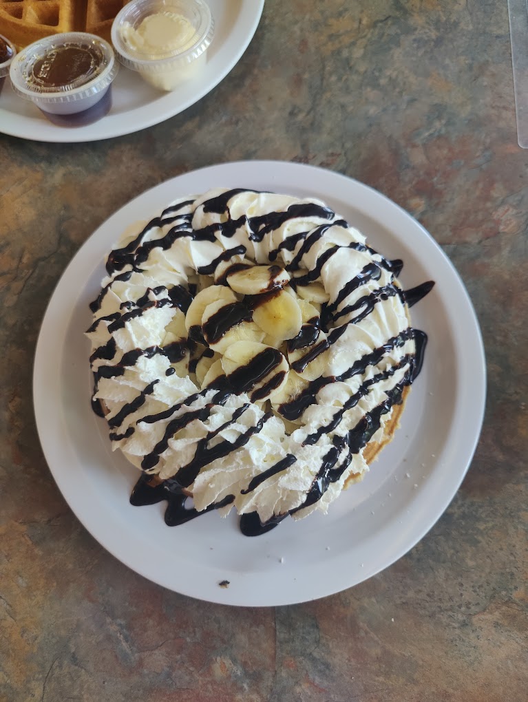 A waffle with whip cream and bananas on top drizzled in chocolate sauce.