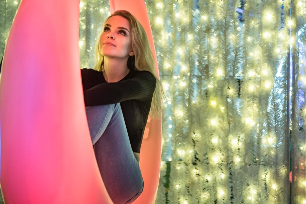 A woman sits on a red light up swing with softly glowing yellow Christmas lights hanging down in the background.