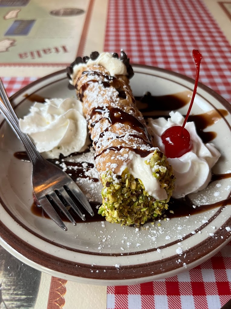 A delicious looking Italian dessert with a cherry on top, nuts, and a chocolate drizzle.