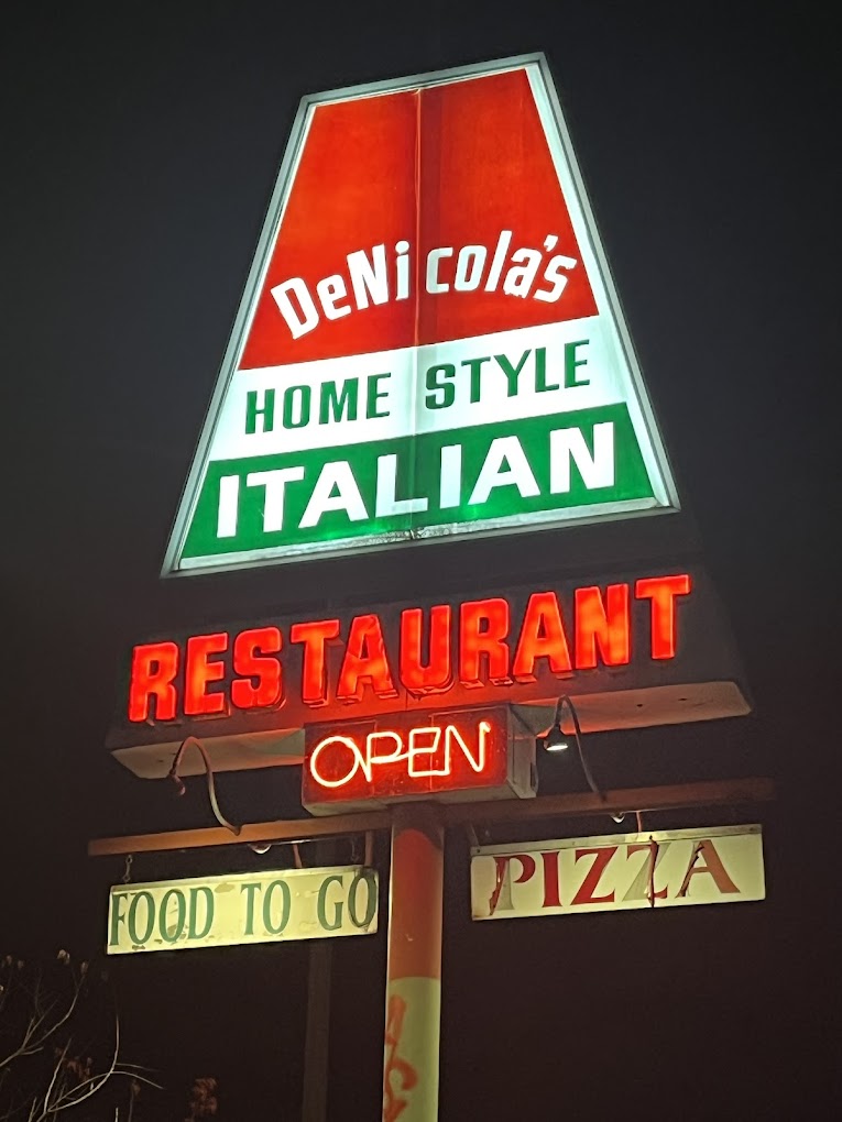 A large red, white, and green light up sign at night outside of DeNicola's.