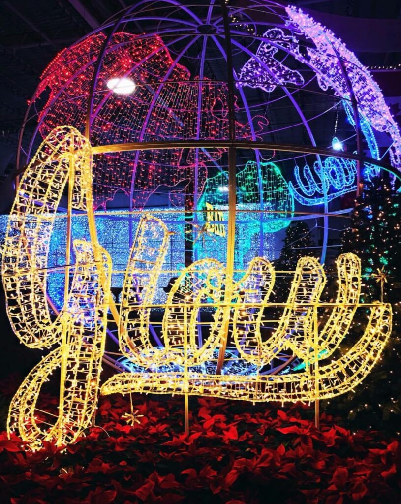 An enormous light up globe with the word 'Glow' written in Christmas lights in front of it.