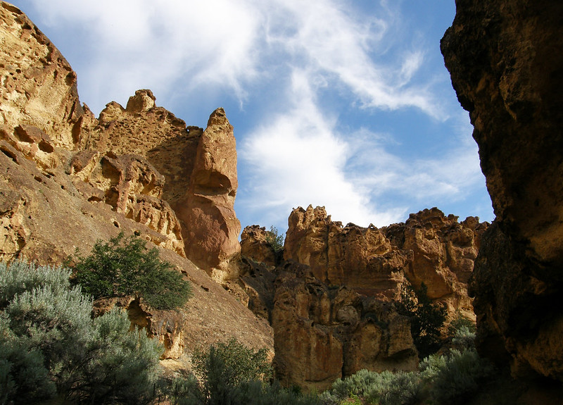 Towering rock monoliths and cliffs reach up towards a blue sky with wispy clouds.