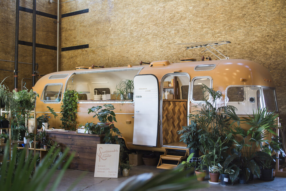 An up close shot of an orange retro Airstream trailer surrounded by green plants.