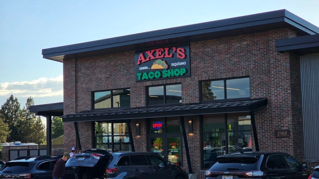 The outside of Axel's Taco Shop. It's a brick building with a large red and green sign on the front.