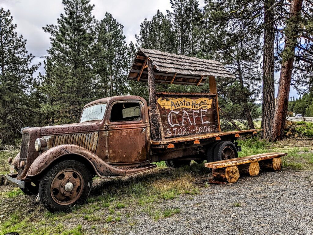 An old rusted out truck with a sign for Austin House on the back of it.