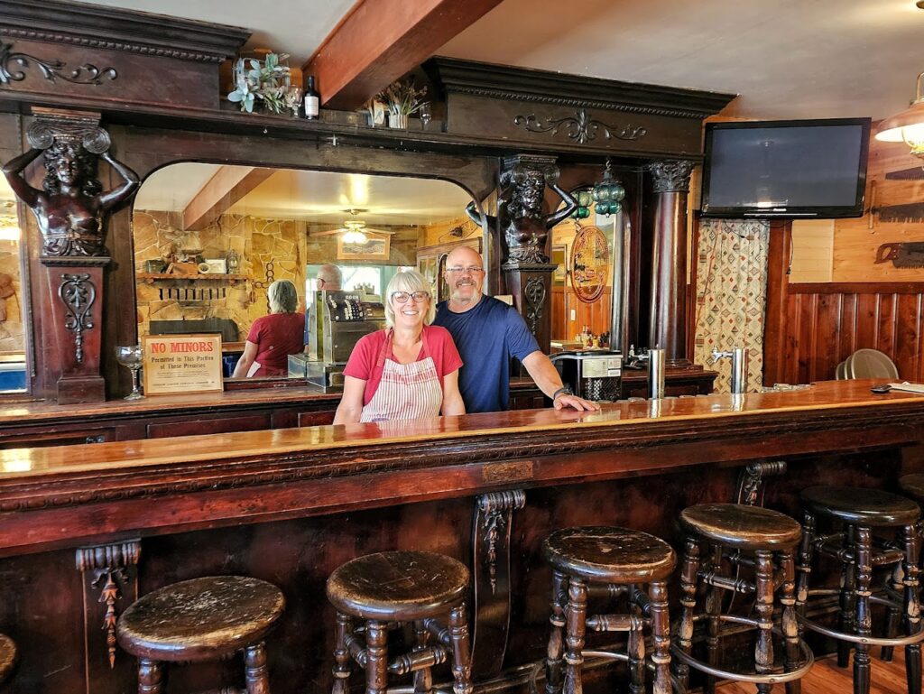 The owners of Austin House stand behind the historic wood bar, smiling at the camera.